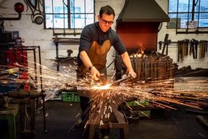 a man holds metal over an anvil as sparks fly